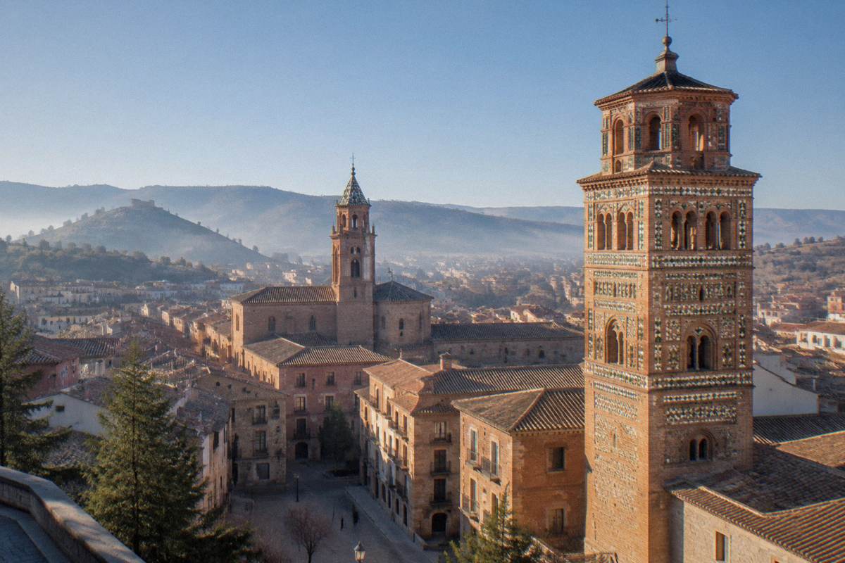 A tall Mudejar brick tower rising above the rooftops of a hill town